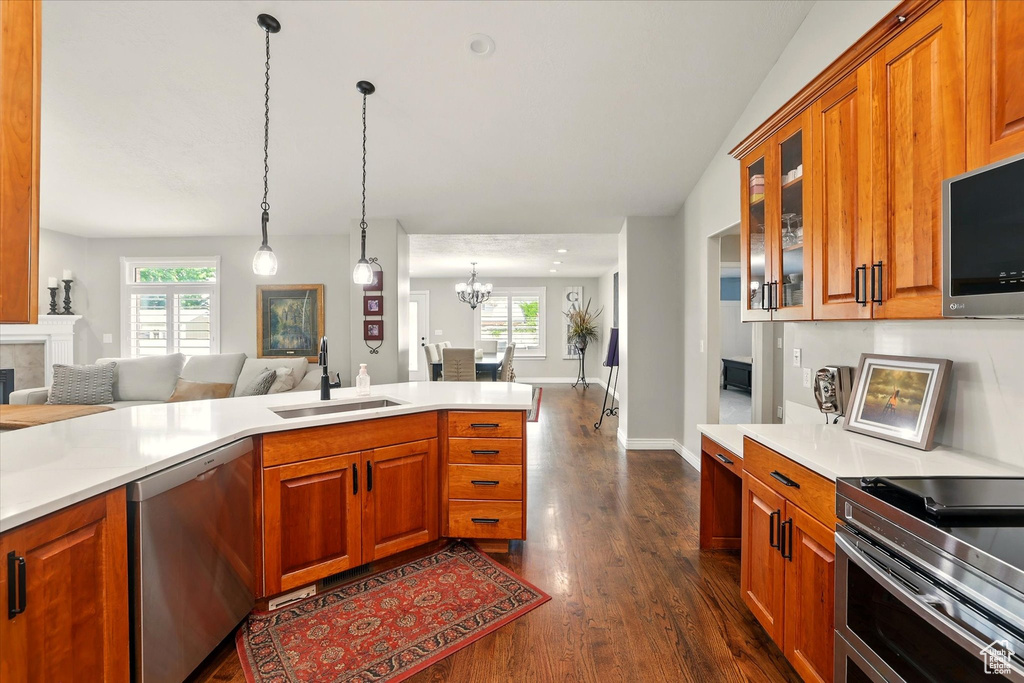 Kitchen featuring appliances with stainless steel finishes, a sink, open floor plan, dark wood finished floors, and a chandelier