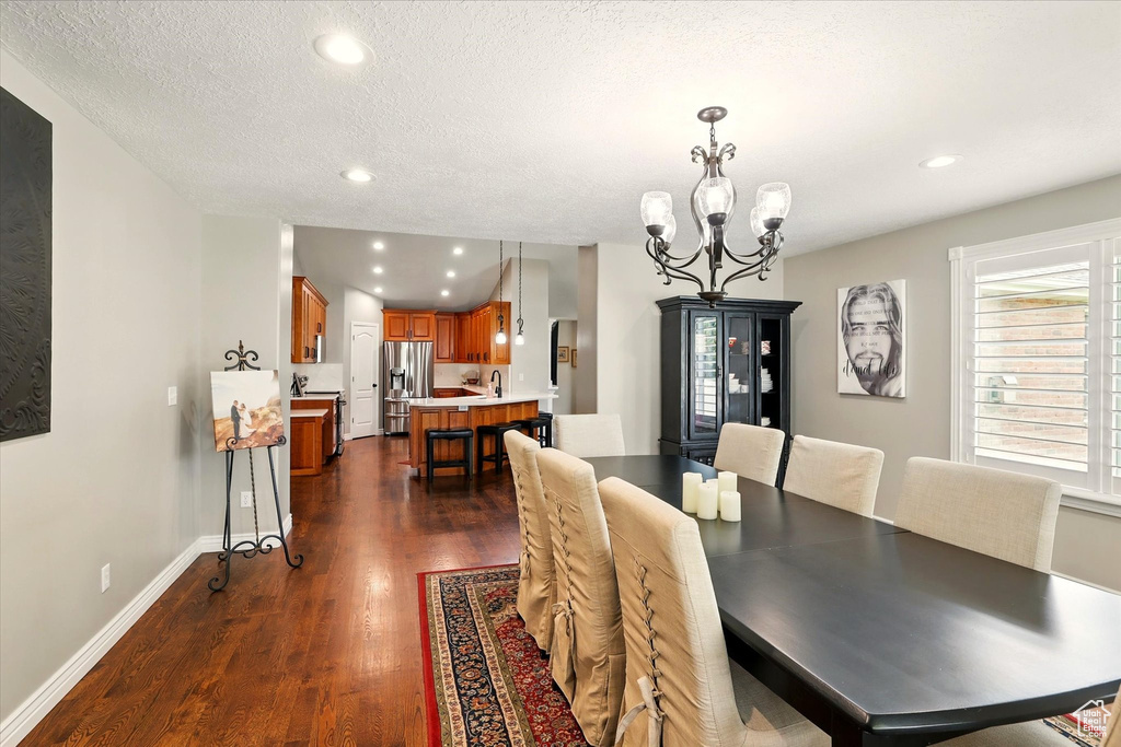 Dining room featuring dark wood-style flooring, a chandelier, recessed lighting, baseboards, and a textured ceiling