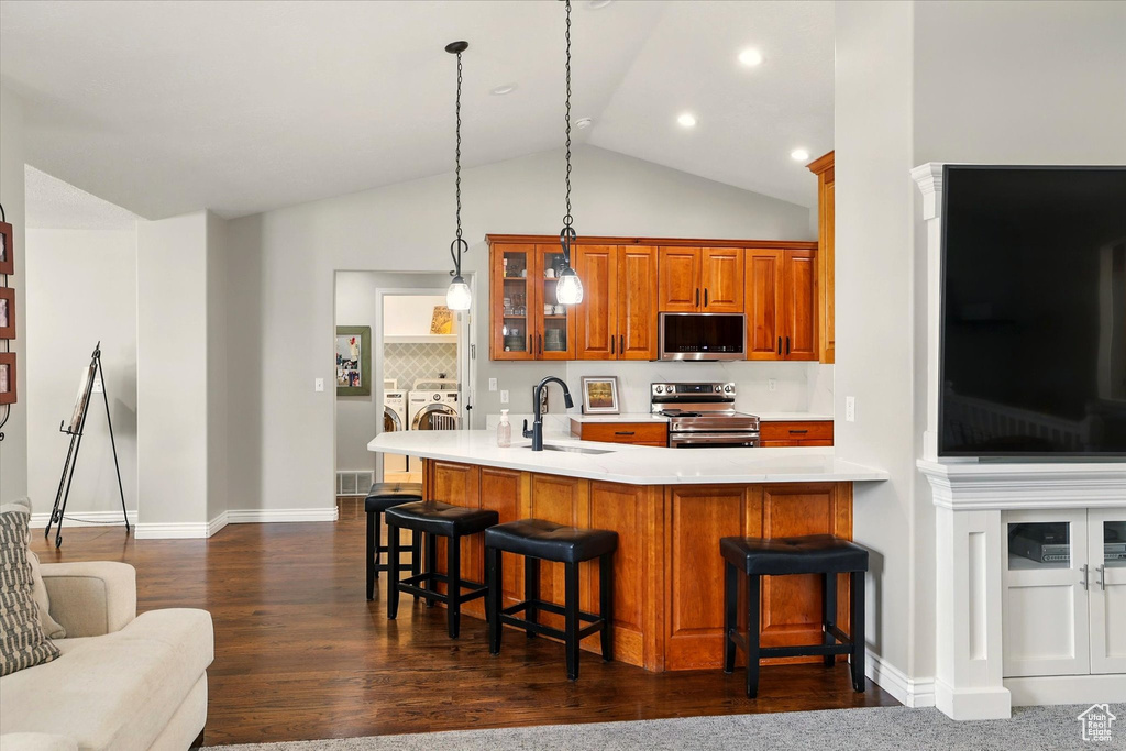 Kitchen featuring appliances with stainless steel finishes, washing machine and clothes dryer, a sink, brown cabinetry, and glass insert cabinets