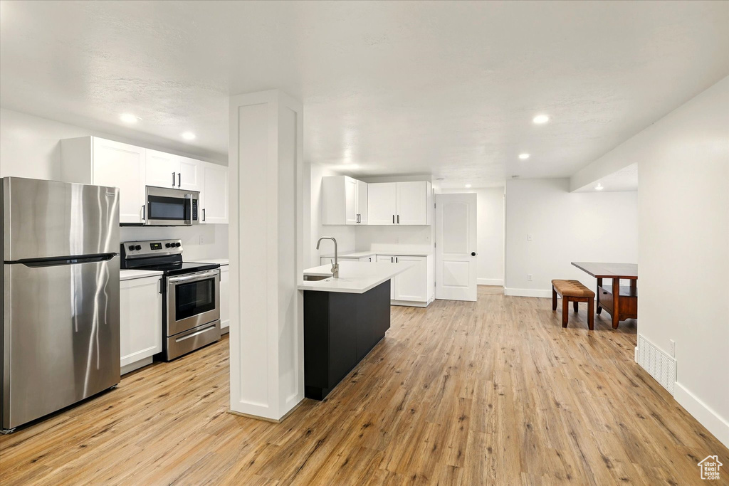 Kitchen featuring stainless steel appliances, light wood finished floors, light countertops, white cabinetry, and recessed lighting