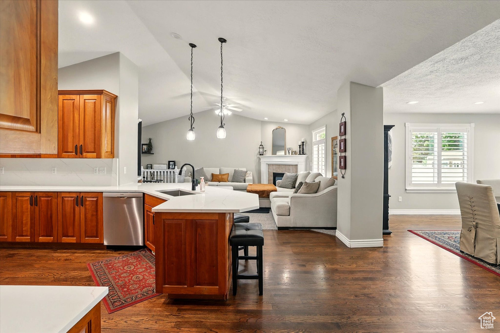 Kitchen with stainless steel dishwasher, a sink, a peninsula, dark wood-style floors, and lofted ceiling