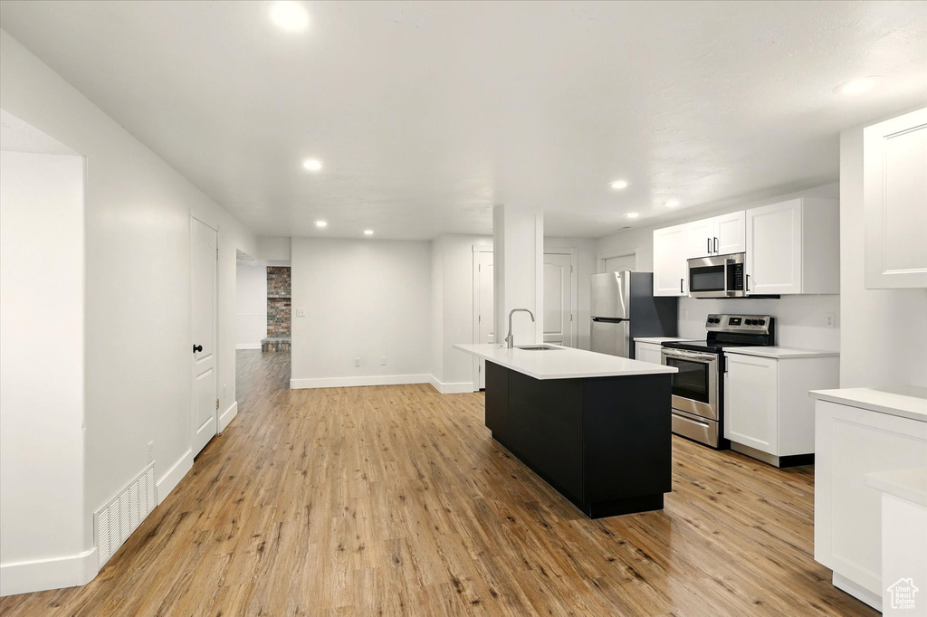 Kitchen with appliances with stainless steel finishes, a sink, recessed lighting, light wood-style flooring, and light countertops