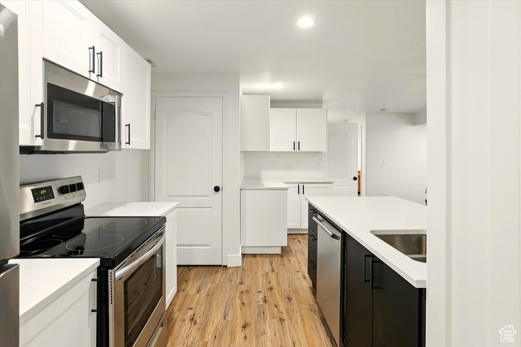Kitchen with appliances with stainless steel finishes, light wood-style flooring, white cabinetry, a sink, and light countertops