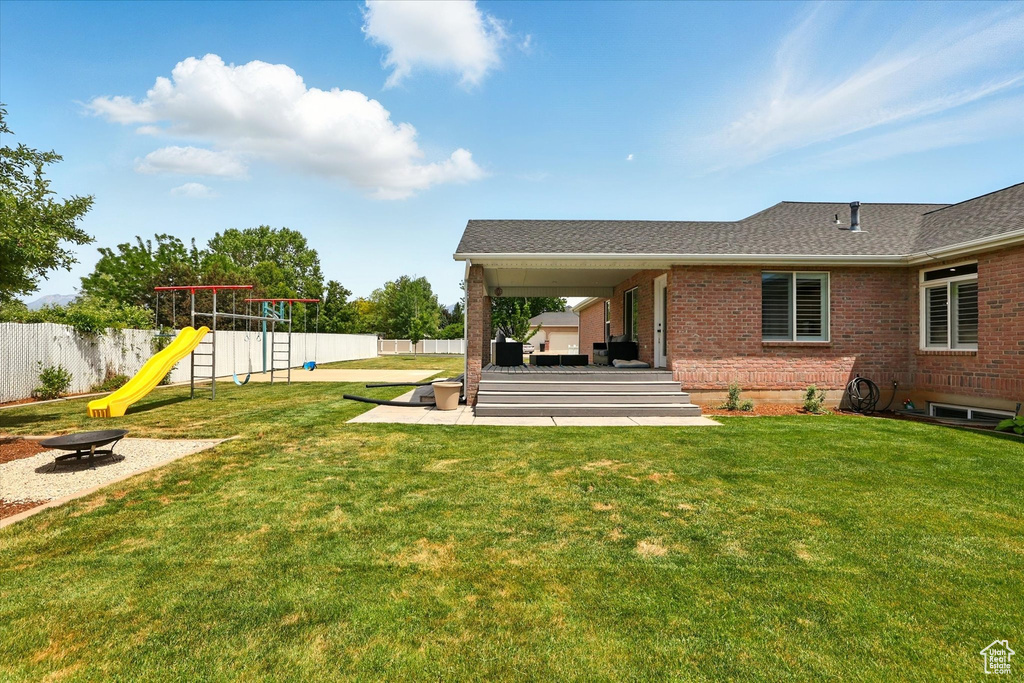 Back of property with a fire pit, a playground, brick siding, a patio, and roof with shingles
