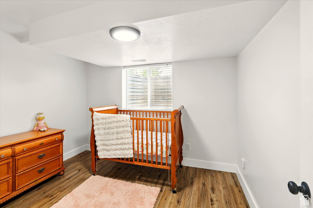 Bedroom featuring baseboards, wood finished floors, and a crib