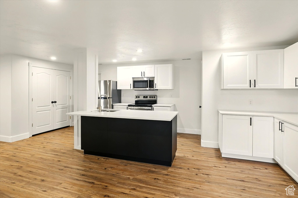 Kitchen with stainless steel appliances, recessed lighting, white cabinetry, light wood finished floors, and baseboards