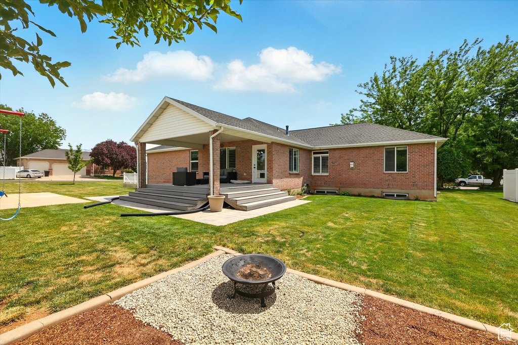 Rear view of property featuring a fire pit, brick siding, a lawn, and a patio