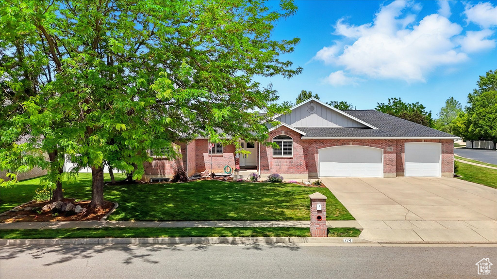 View of front of home featuring a garage, concrete driveway, brick siding, a front lawn, and roof with shingles