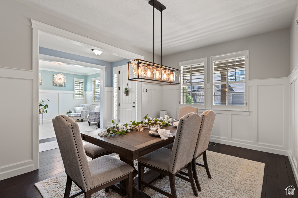 Dining space with a decorative wall, dark wood-style floors, wainscoting, and a chandelier