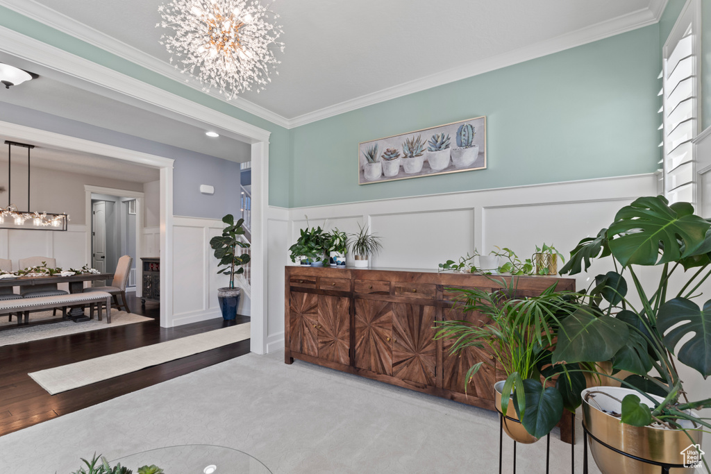 Corridor featuring a chandelier, ornamental molding, a decorative wall, and a wainscoted wall