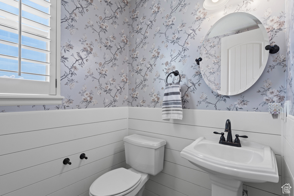 Half bathroom with wallpapered walls, a wainscoted wall, toilet, and a sink