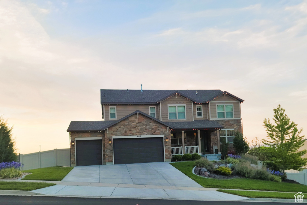 View of front facade featuring a porch, an attached garage, stone siding, and concrete driveway