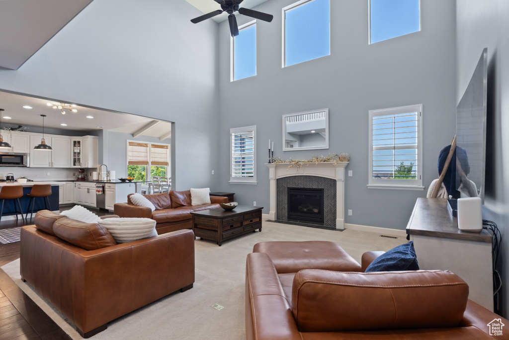 Living room featuring a towering ceiling, ceiling fan, a fireplace with flush hearth, plenty of natural light, and baseboards