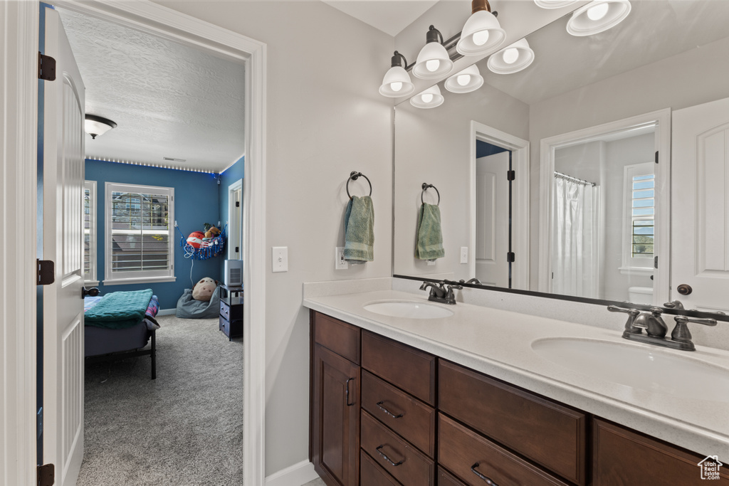Full bathroom with double vanity, plenty of natural light, baseboards, a textured ceiling, and curtained shower