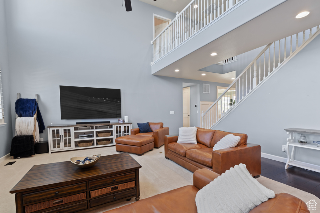 Living area with stairs, a towering ceiling, ceiling fan, baseboards, and wood finished floors