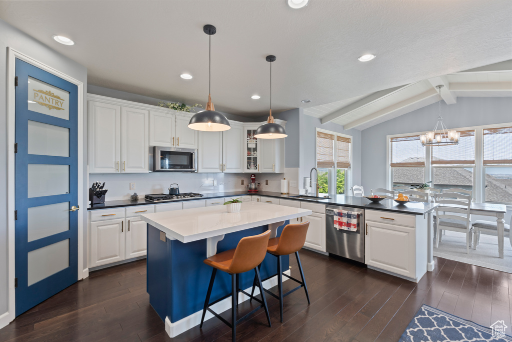 Kitchen with a peninsula, appliances with stainless steel finishes, a sink, dark wood-type flooring, and a chandelier