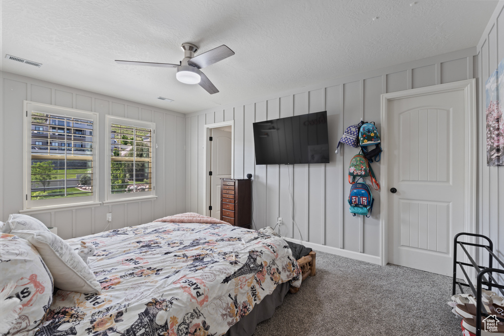 Bedroom featuring carpet flooring, a textured ceiling, ceiling fan, and a decorative wall