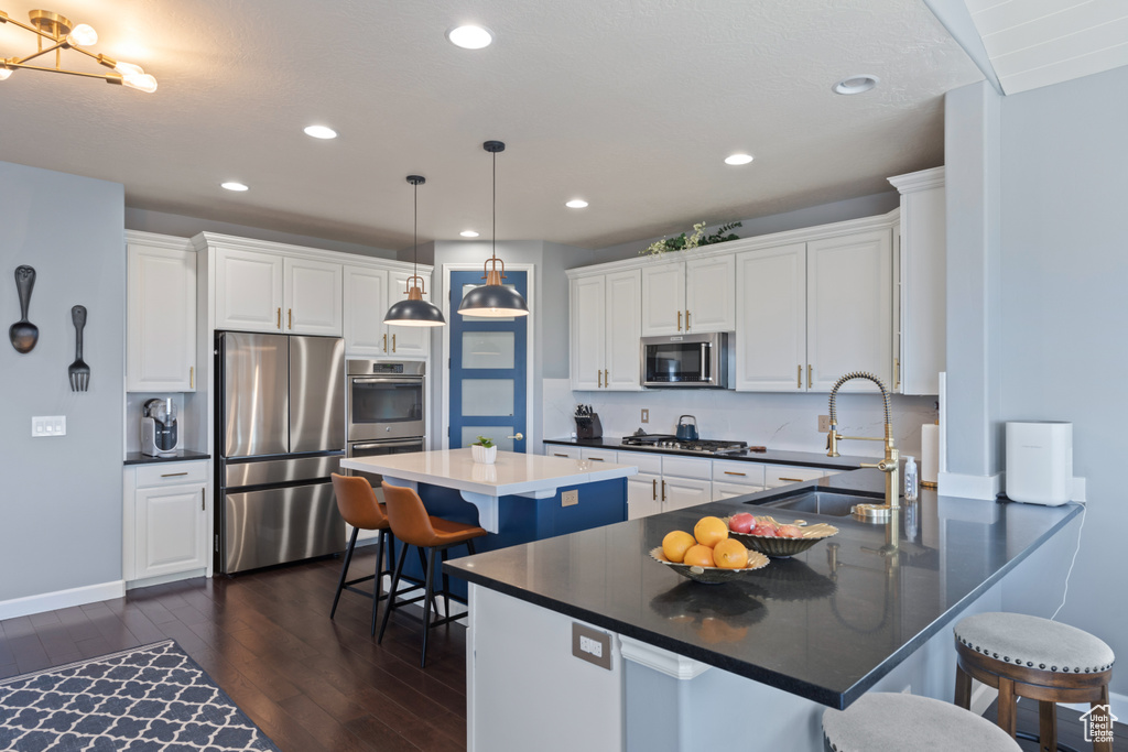 Kitchen with stainless steel appliances, dark wood-style floors, a sink, a peninsula, and white cabinetry