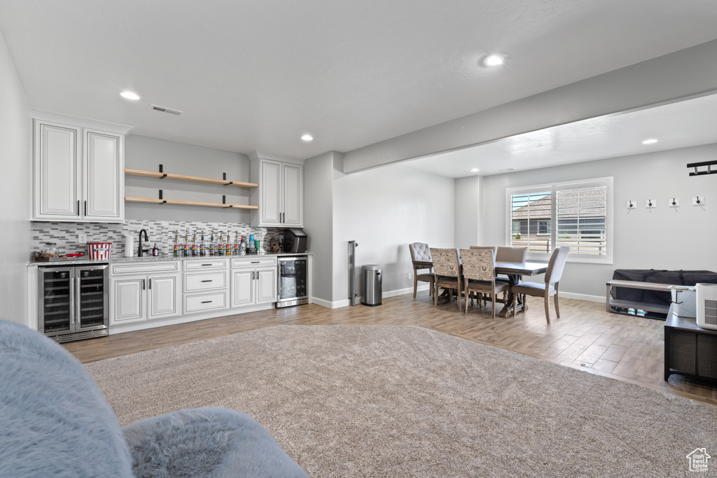 Indoor wet bar featuring beverage cooler, light wood-style floors, tasteful backsplash, recessed lighting, and baseboards