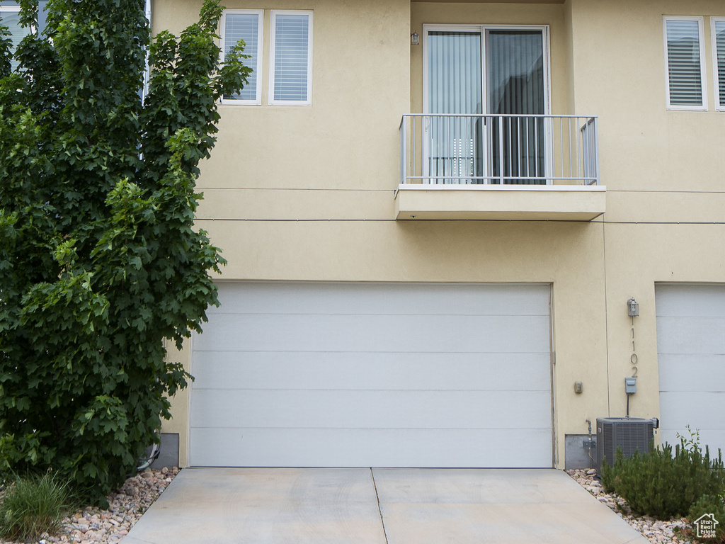 View of property featuring a garage, stucco siding, concrete driveway, and central air condition unit