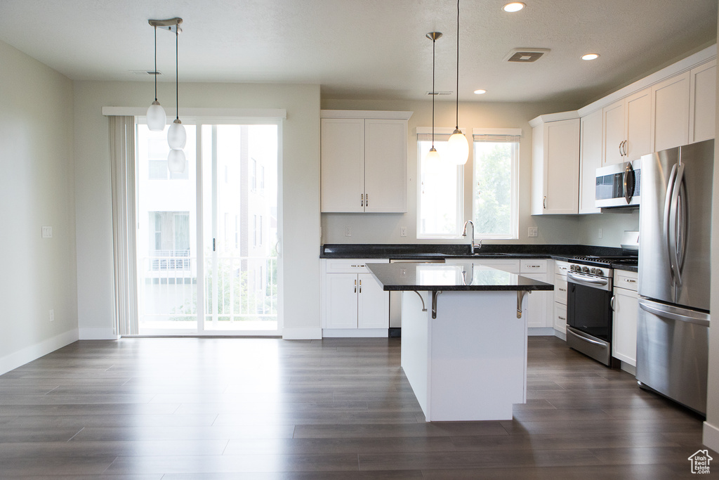 Kitchen featuring appliances with stainless steel finishes, dark countertops, recessed lighting, a kitchen bar, and white cabinetry