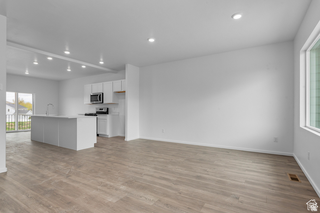 Kitchen with appliances with stainless steel finishes, light wood-style flooring, white cabinetry, recessed lighting, and a center island with sink