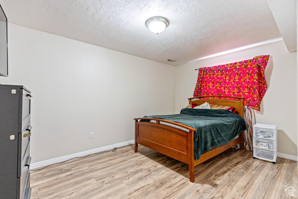Bedroom featuring light wood finished floors, a textured ceiling, and baseboards
