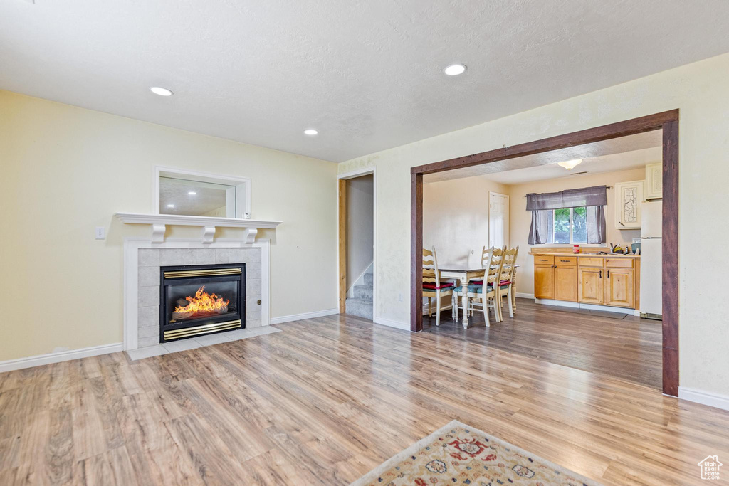 Living area with light wood finished floors, a tile fireplace, recessed lighting, stairway, and baseboards