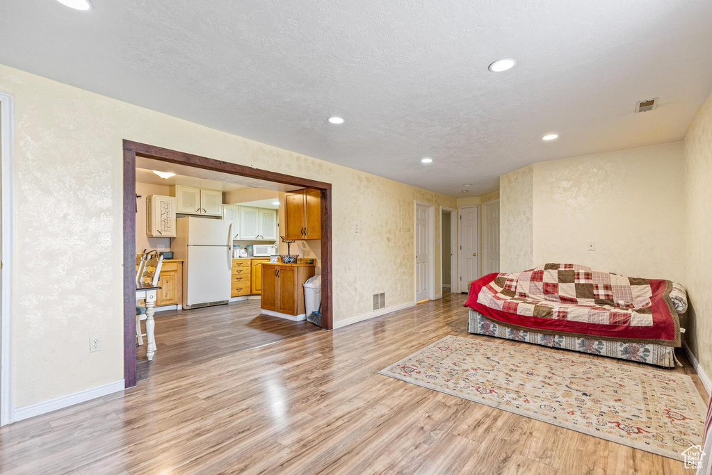 Living area with light wood finished floors, baseboards, recessed lighting, and a textured wall