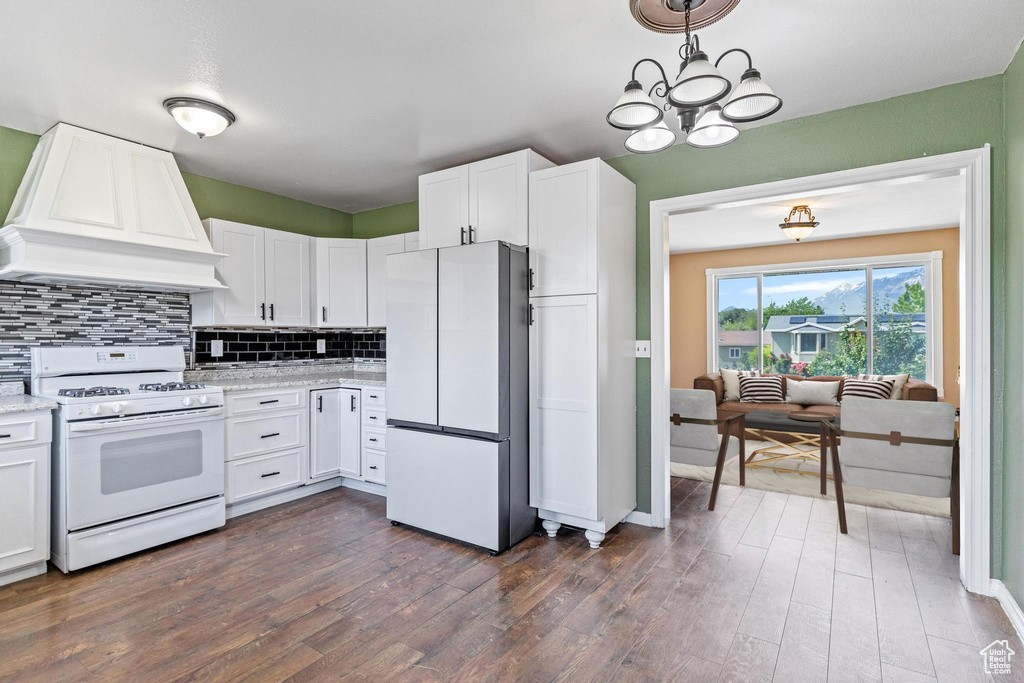 Kitchen with white appliances, premium range hood, tasteful backsplash, and white cabinets