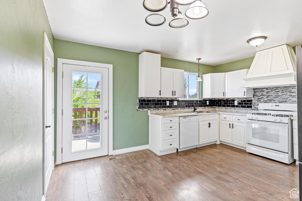 Kitchen with white appliances, custom exhaust hood, decorative backsplash, and plenty of natural light