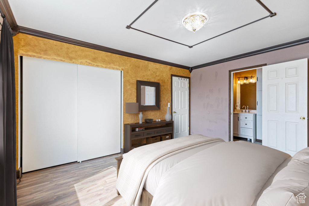 Bedroom with a chandelier, light wood-type flooring, ornamental molding, and connected bathroom