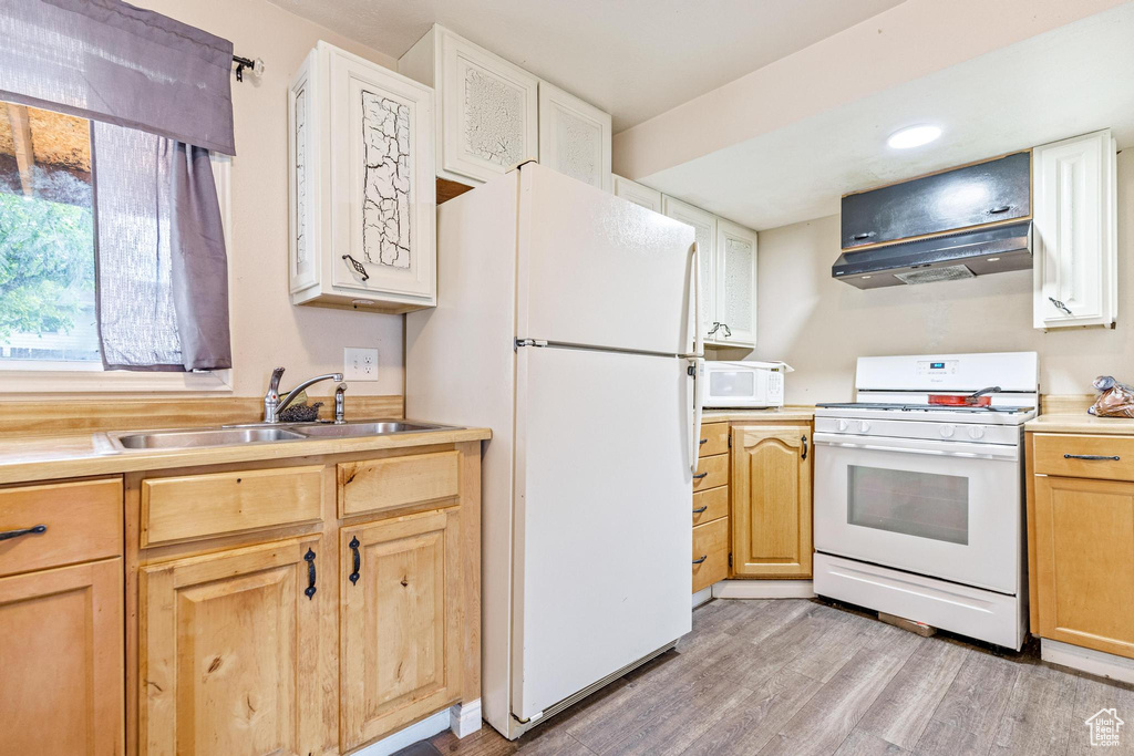 Kitchen featuring white appliances, a sink, light wood finished floors, under cabinet range hood, and light countertops