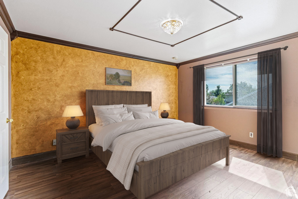 Bedroom with crown molding, baseboards, an accent wall, wood finished floors, and a chandelier
