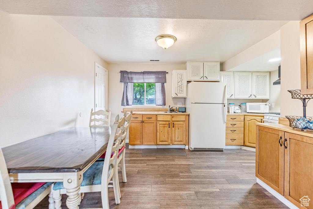Kitchen featuring white appliances, wood finished floors, light countertops, a sink, and wall chimney exhaust hood