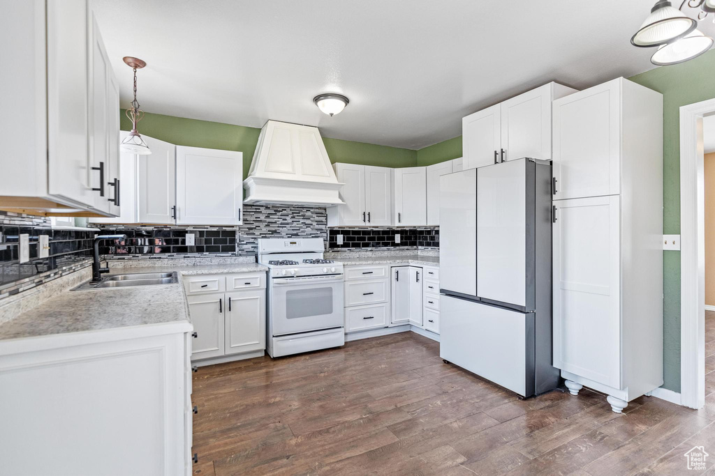 Kitchen with white appliances, premium range hood, a sink, tasteful backsplash, and dark wood finished floors