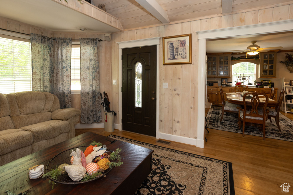 Living area featuring beamed ceiling, wood finished floors, plenty of natural light, a ceiling fan, and wood walls