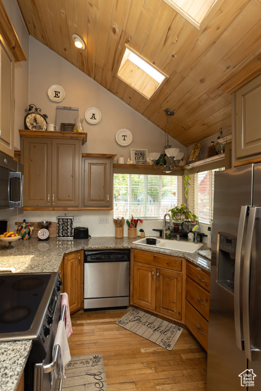 Kitchen featuring appliances with stainless steel finishes, a sink, vaulted ceiling, healthy amount of natural light, and light wood-type flooring
