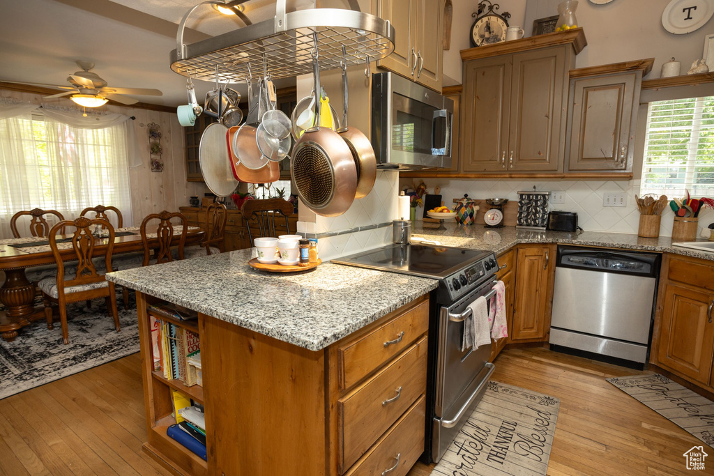 Kitchen with appliances with stainless steel finishes, light wood finished floors, backsplash, and a ceiling fan