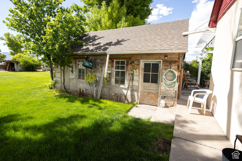 View of front of house featuring a shingled roof, a front lawn, an outbuilding, and stone siding