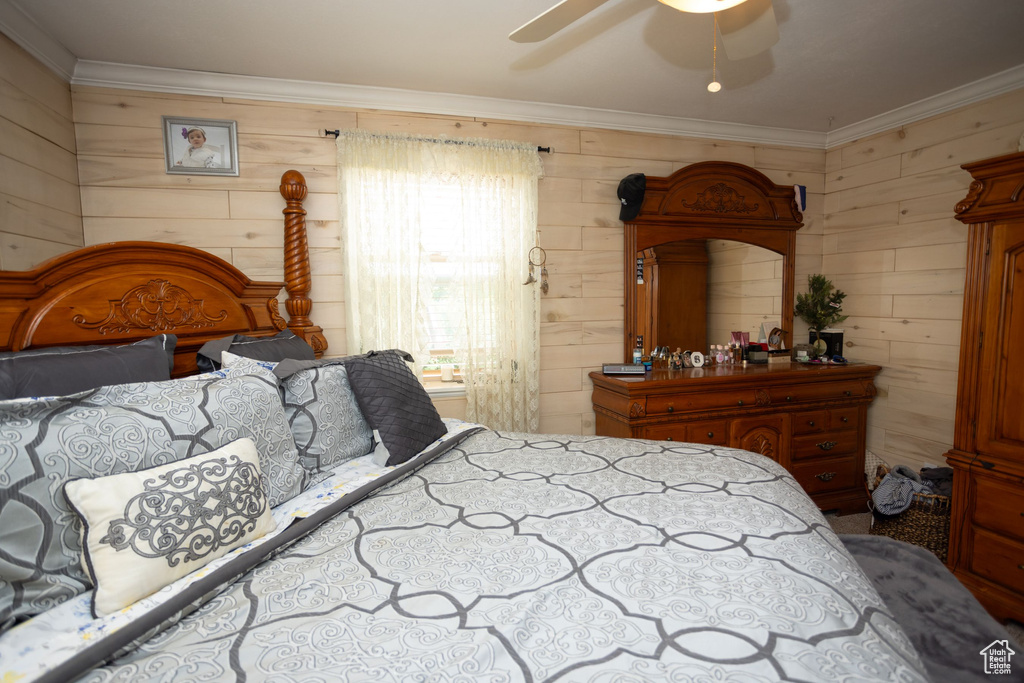 Bedroom featuring wooden walls, ornamental molding, and ceiling fan