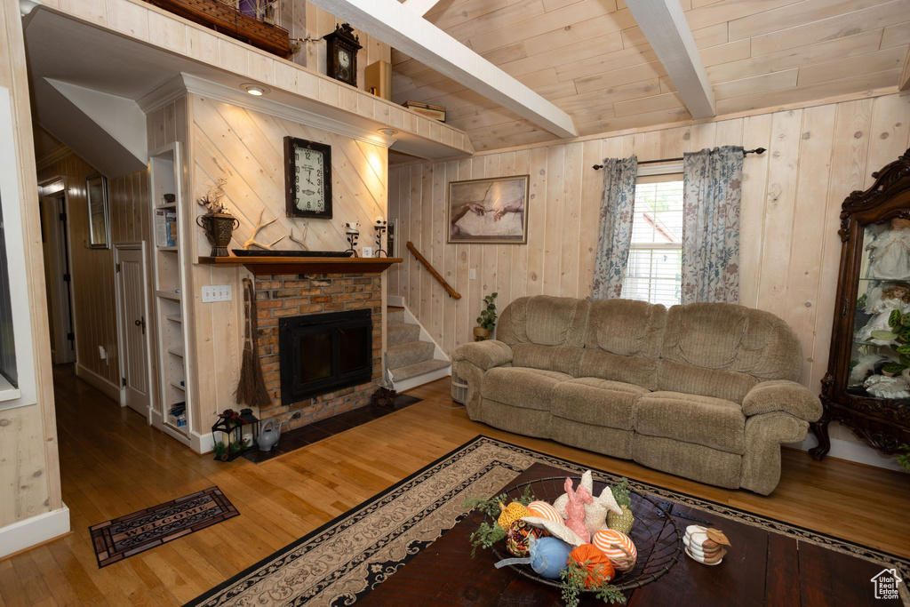 Living area featuring a brick fireplace, wood finished floors, wood ceiling with exposed beams, wooden walls, and stairs