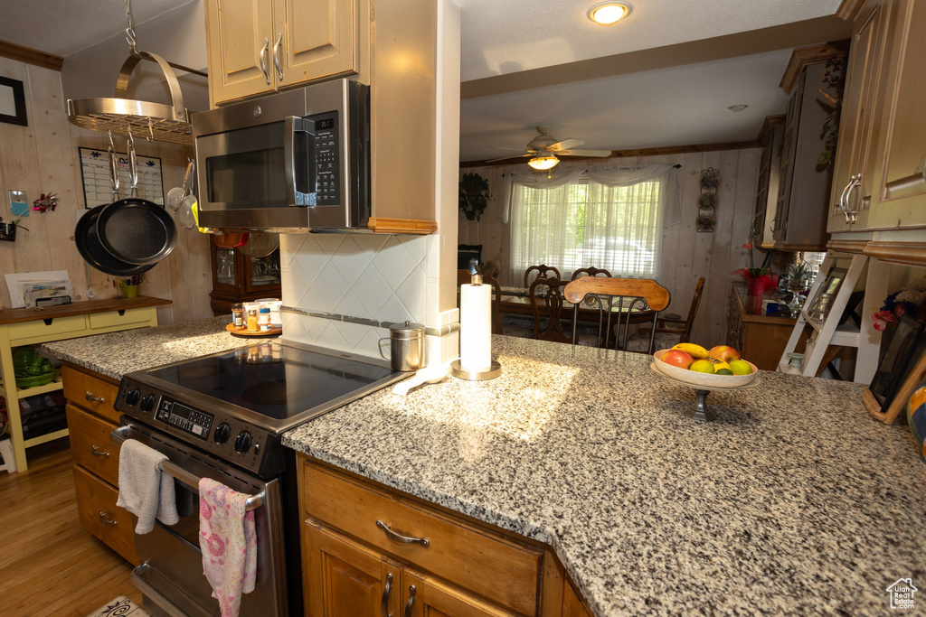 Kitchen featuring stainless steel microwave, electric stove, ceiling fan, light stone countertops, and backsplash