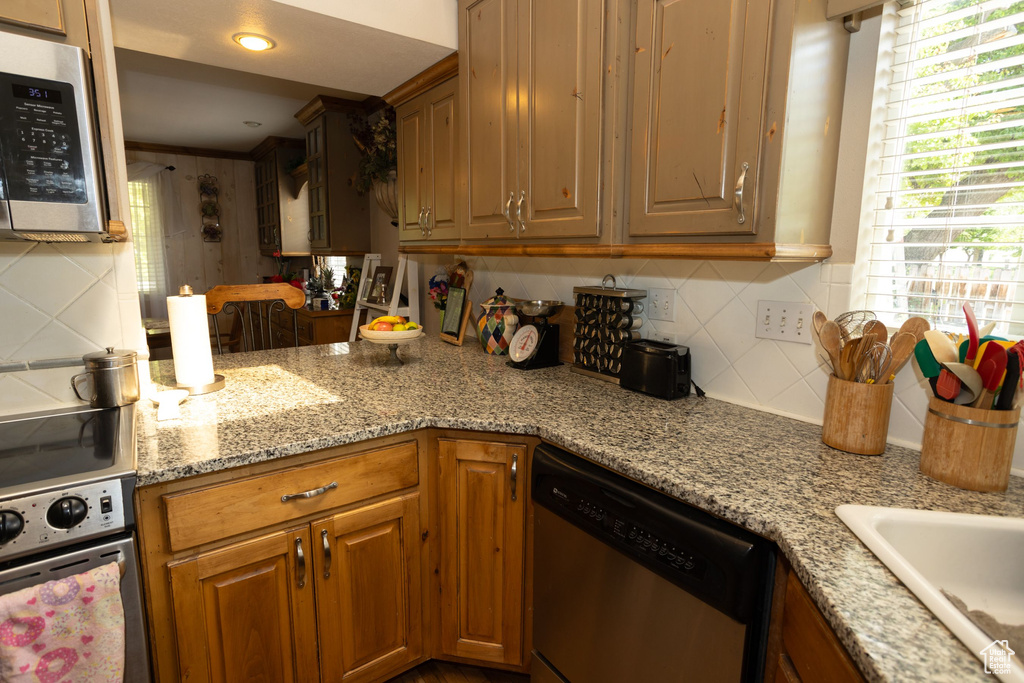 Kitchen with stainless steel appliances, decorative backsplash, light stone countertops, a sink, and brown cabinets