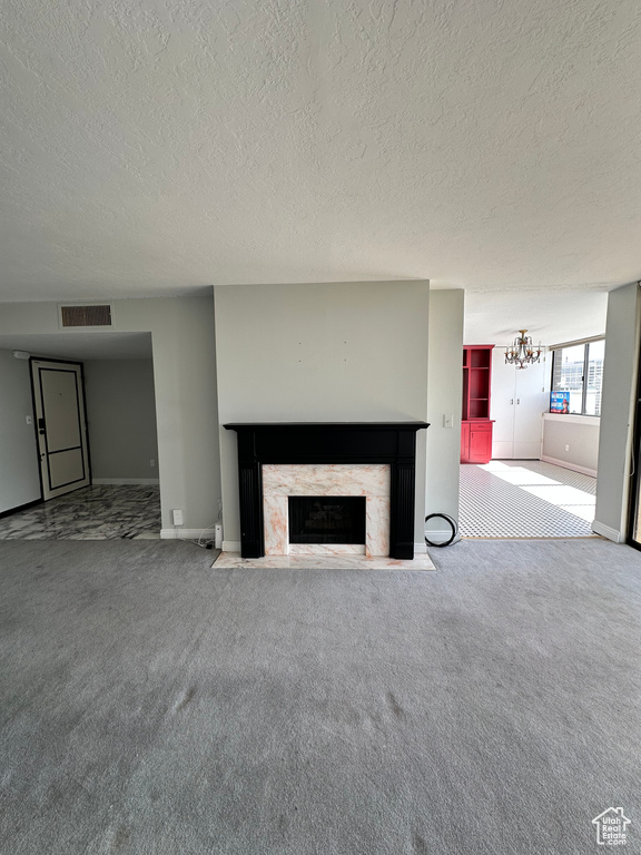 Unfurnished living room featuring carpet flooring, a fireplace, a textured ceiling, baseboards, and a chandelier