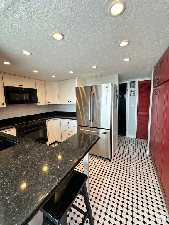 Kitchen featuring freestanding refrigerator, black microwave, tasteful backsplash, recessed lighting, and a textured ceiling