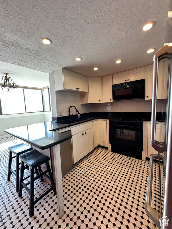 Kitchen featuring black appliances, a sink, dark countertops, backsplash, and a textured ceiling
