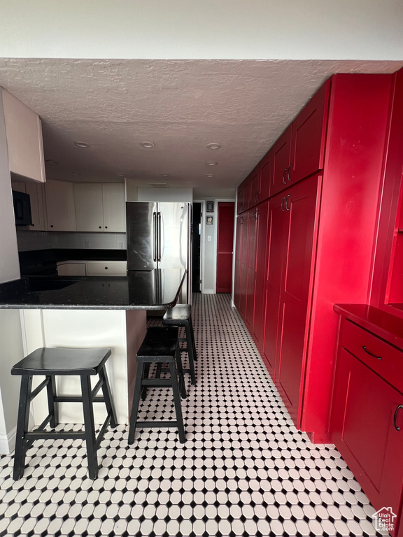 Kitchen with freestanding refrigerator, a textured ceiling, dark countertops, black microwave, and red cabinetry