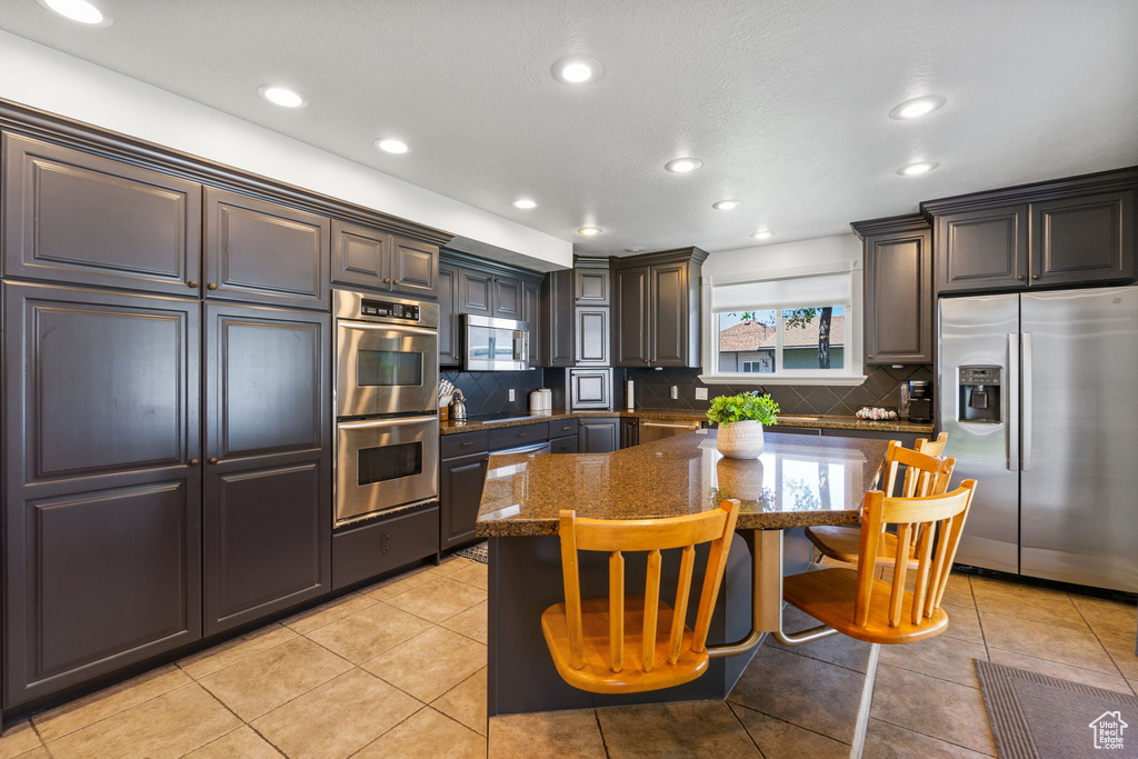 Kitchen with stainless steel appliances, tasteful backsplash, a kitchen bar, dark stone counters, and a center island