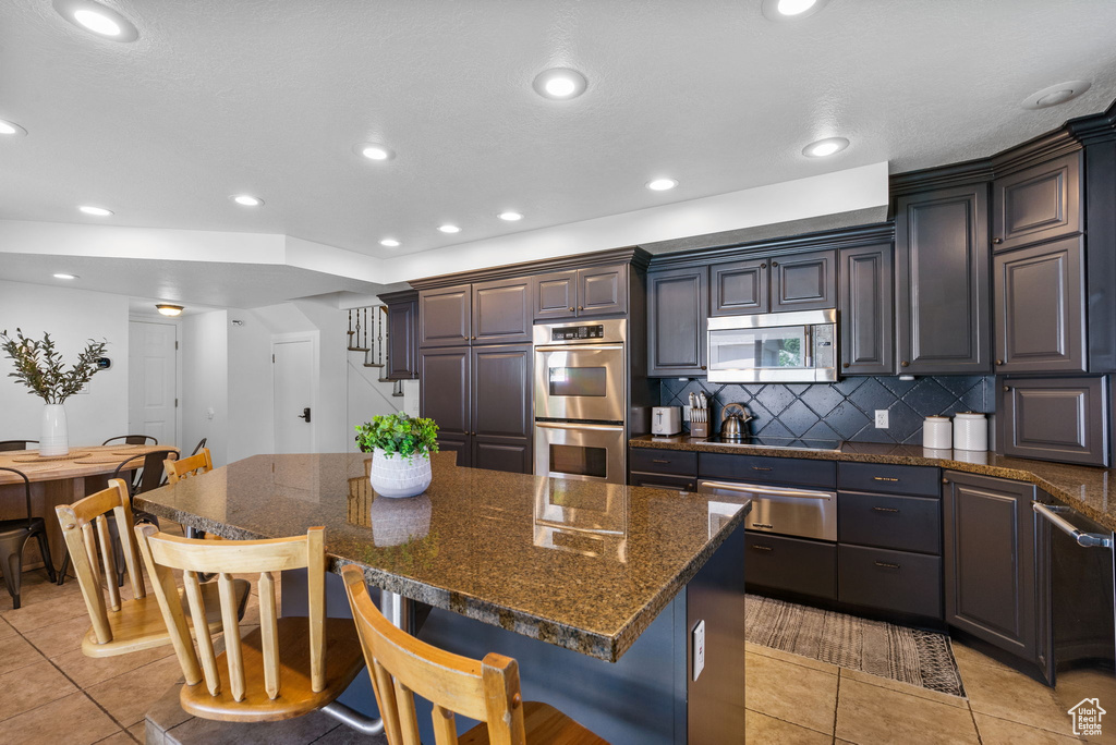 Kitchen featuring stainless steel appliances, a warming drawer, a kitchen breakfast bar, a kitchen island, and light tile patterned flooring
